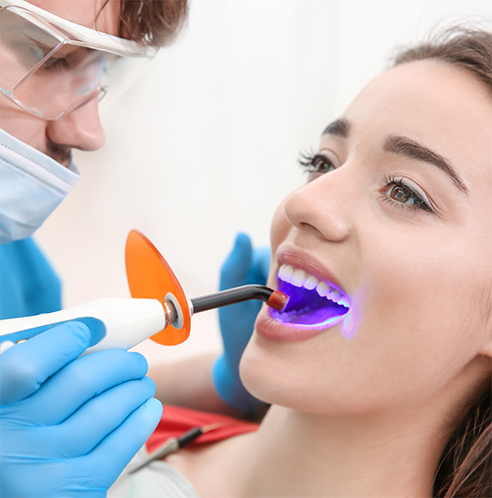 Performing cosmetic dental bonding on woman's lower teeth