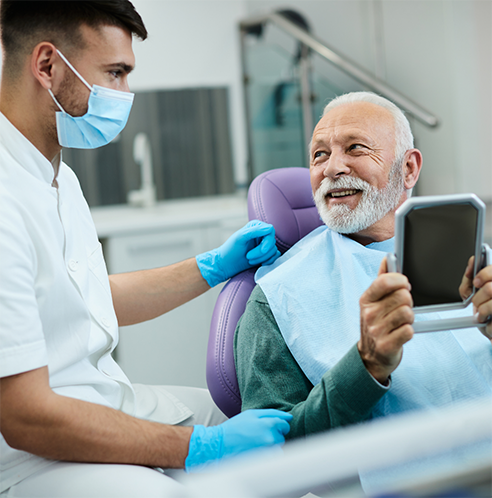 Dentist with mask looking at older male patient
