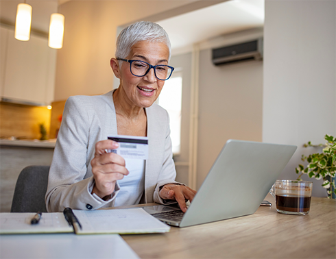 Woman with glasses typing on laptop and looking at credit card
