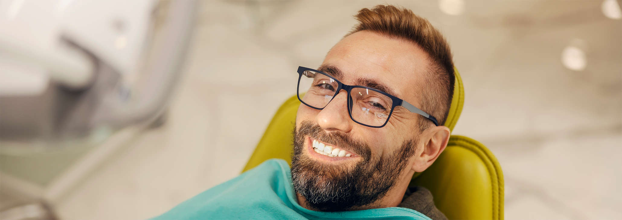 Male patient with glasses leaning back in dental chair smiling