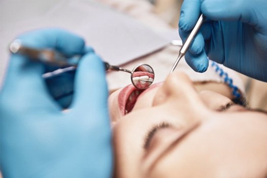 Dentist leaning over patient with instruments to examine her mouth