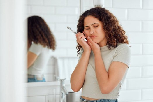 Woman holding her jaw after brushing her teeth