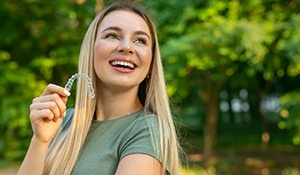 a woman smiling and holding clear aligners