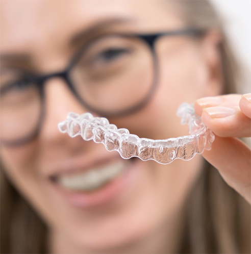 Woman with glasses holding clear aligner