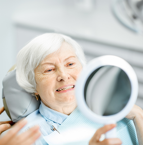Senior woman sitting in dental chair looking at handheld mirror