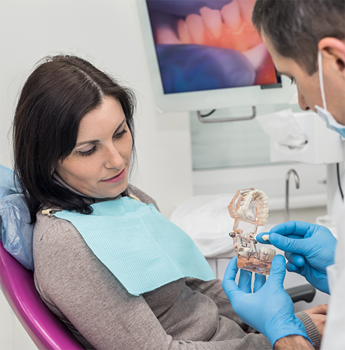 Female patient looking at dentist holding dental crown and model of mouth with dental implants
