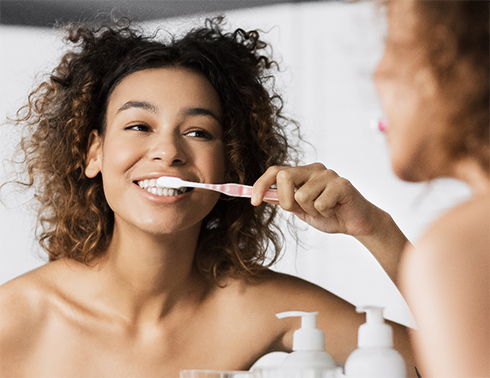 Woman brushing her teeth in bathroom mirror