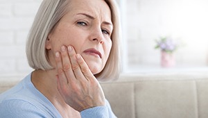 woman holding her face with symptoms of dental implant failure in Midland