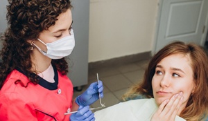 A young woman holding her cheek while a dental hygienist prepares to check her mouth