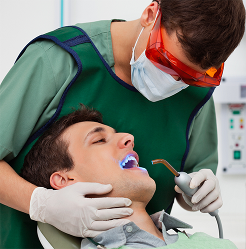 Dentist with mask applying dental sealants to patient's teeth