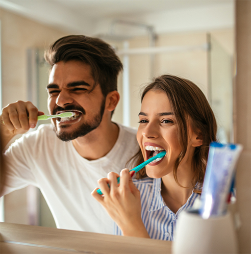 Man and woman brushing teeth in bathroom mirror