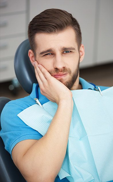 Man in dental chair holding his cheek in pain