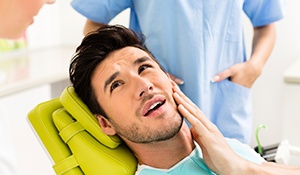 Man in dental chair holding jaw