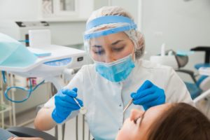 dentist cleaning a patient's teeth while wearing PPE