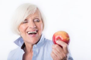 woman holding an apple who needs to learn about eating with dentures