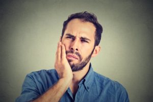 man holding his mouth with a loose dental implant