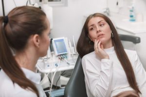 woman holding her face and worried about pain at the dentist’s office