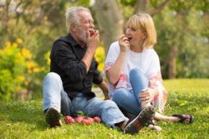 older couple biting into apples at a picnic